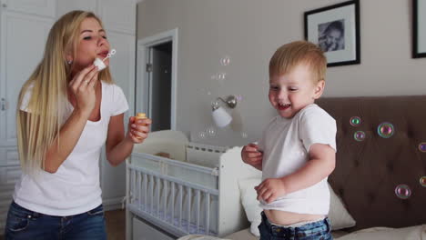 the boy and mom are playing with soap bubbles on the bed in the bedroom in slow motion