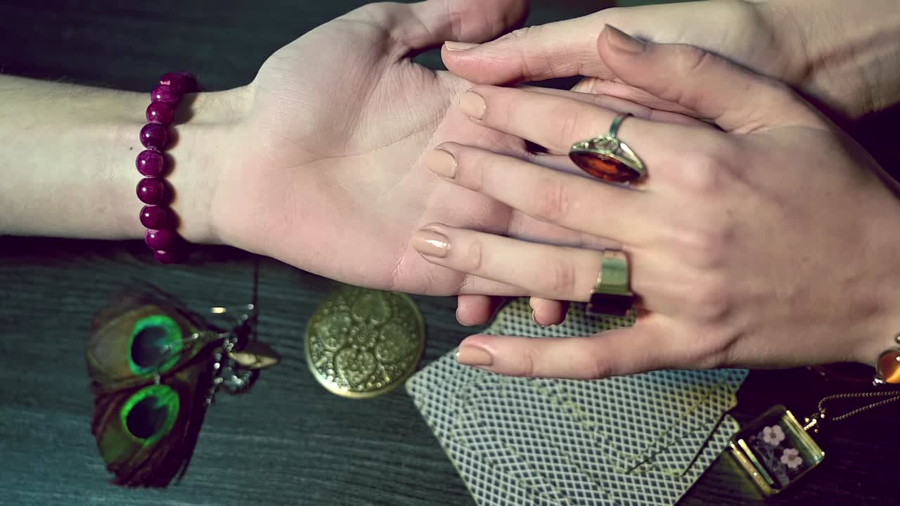 Fortune teller hands reading fortune lines on male palm above table with cards and esoteric jewelry. Overhead shot. Slow motion