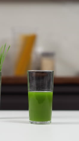 un vaso fresco de jugo de hierba de trigo en un mostrador de la cocina con un jarrón de hierbas de trigo en el fondo