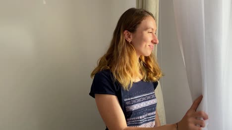 Mujer-Mira-Por-Una-Ventana-Sonriendo-En-Casa