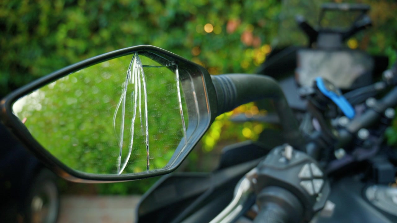 Motocicletta con uno specchietto retrovisore rotto che riflette uno sfondo verde sfocato, evidenziando il danno e la necessità di riparazione.