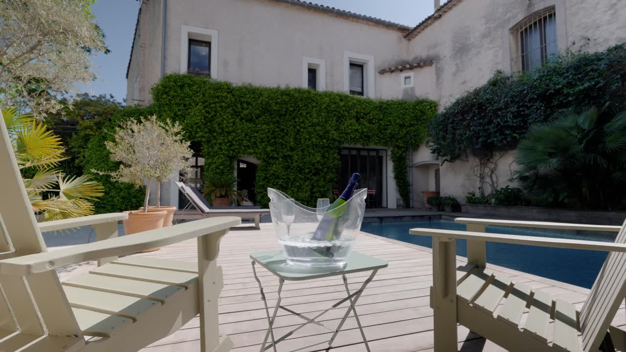 Ripresa orbitale di una villa con lettini prendisole e una bottiglia di vino a bordo piscina