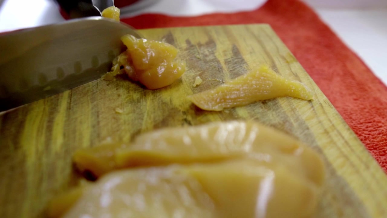Primo piano di un coltello affilato che taglia un filetto di pollo crudo fresco a striscioline su un tagliere di legno rustico per una ricetta di pollo al limone