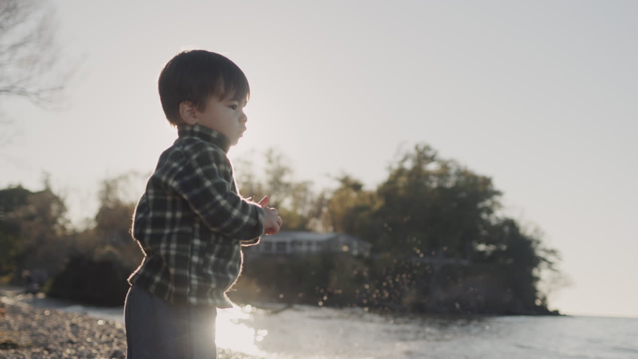 2살 의 의도적 인 소년 이 바다 에 돌 을 던진다. 뒤쪽 시선, 느린 동작 비디오
