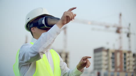 portrait of a male inspector analyzing the work of builders using virtual reality glasses. a man in a helmet and a protective vest stands in vr glasses and moves his hands.