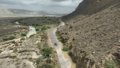 Aerial-View-Of-Vehicle-Driving-Along-Empty-Road-Through-Arid-Desert-Land-At-Hingol-National-Park