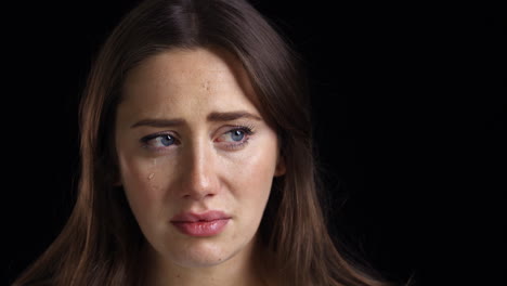 studio shot of unhappy young woman crying into camera