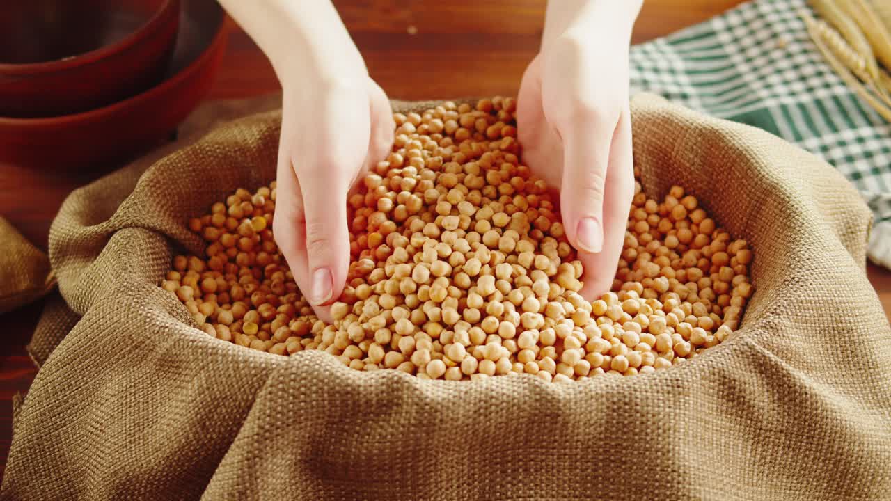 Hands scooping and pouring chickpeas into a burlap sack