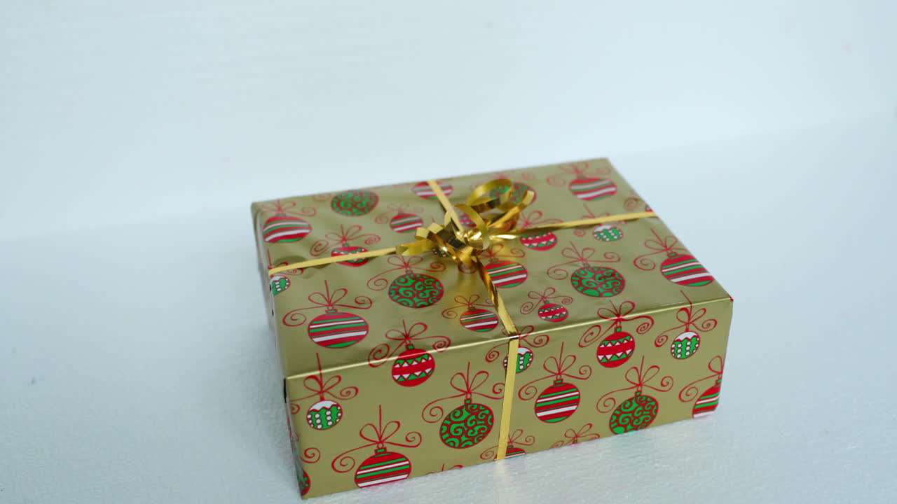 Hands lifting and laying a golden Christmas or birthday wrapped gift in gold foil and white ribbon on party box on white background in real speed motion at 24fps