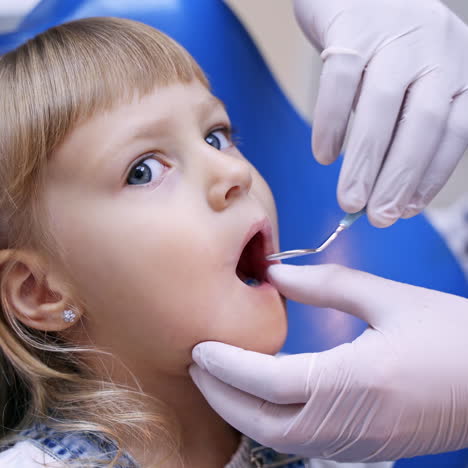 Little girl with opened mouth in the dentist chair. Doctor in protective gloves doing check up of a child's teeth. Close-up.