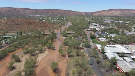 muddy water of todd river with green trees - vehicles driving at stott terrace bridge - remote town of alice springs in northern territory, australia