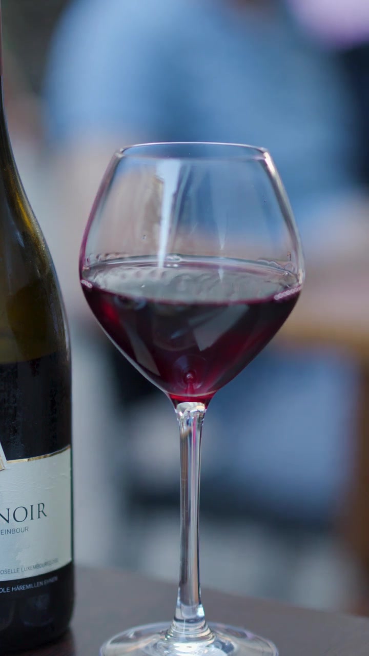 Bicchiere e bottiglia di vino rosso su un tavolo, profondità di campo ridotta, luce naturale soffusa