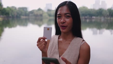 woman using credit card and mobile phone in a park