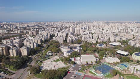 large skate park with grass and trees around, a basketball court and schools with the sea in the background - high altitude shot