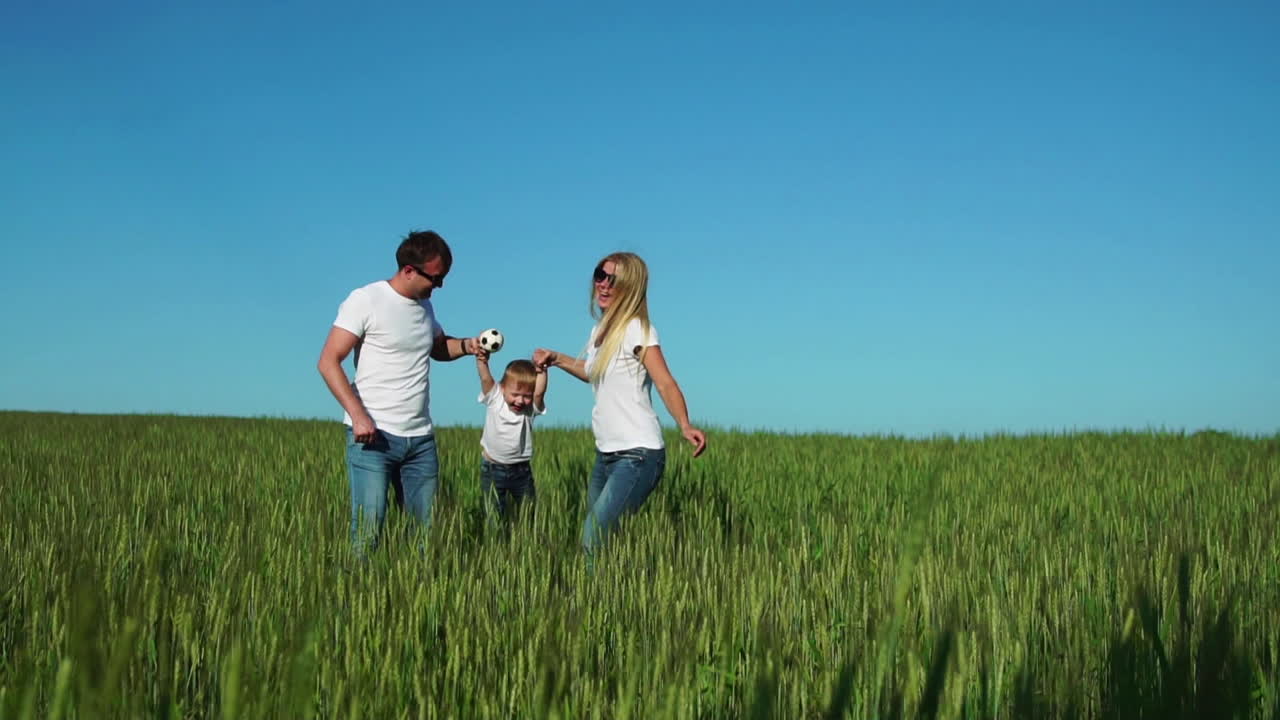 familia feliz: padre madre e hijo saltando y riendo en el campo con camisetas blancas y vaqueros