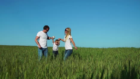 familia feliz: padre madre e hijo saltando y riendo en el campo con camisetas blancas y vaqueros