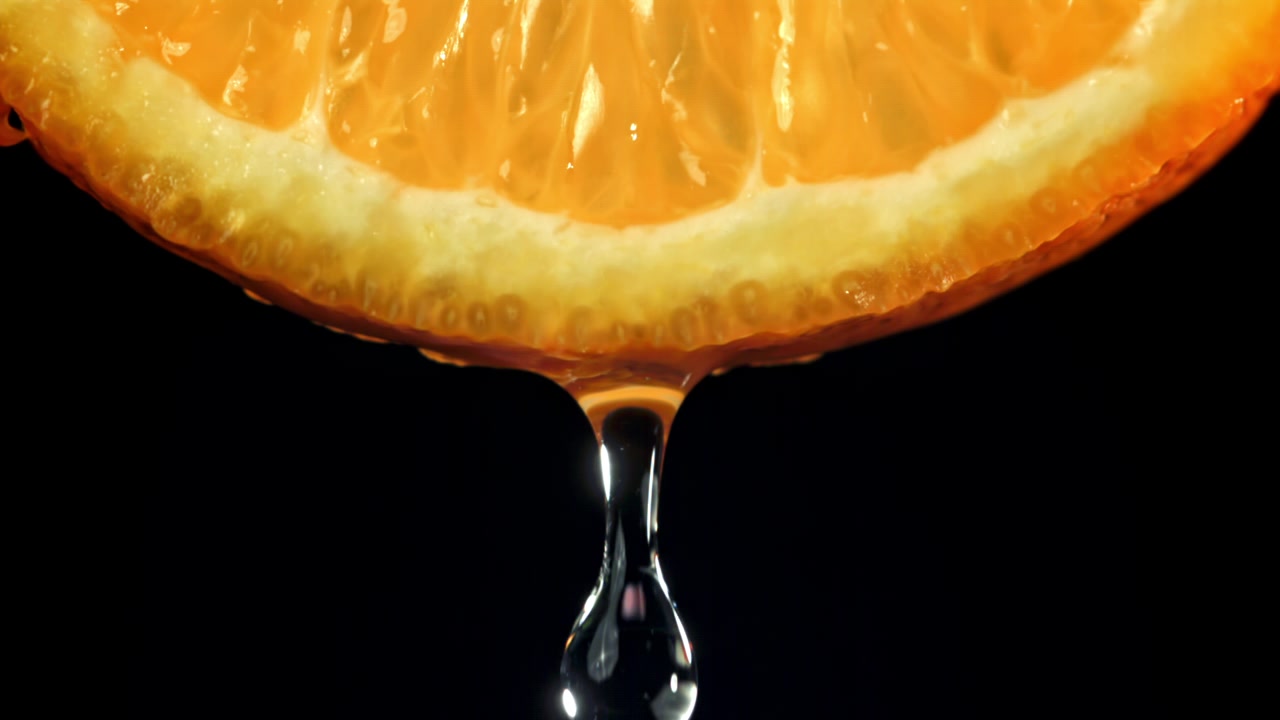 Primo piano al rallentatore di succo che gocciola da una fetta d'arancia fresca