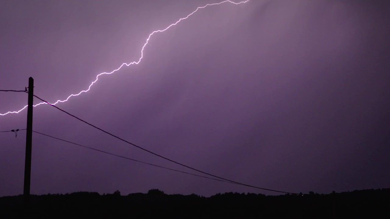 Intenso fulmine attraversa un cielo scuro, illuminando linee elettriche in silhouette in questo drammatico filmato statico di tempesta notturna. Perfetto per temi meteorologici.