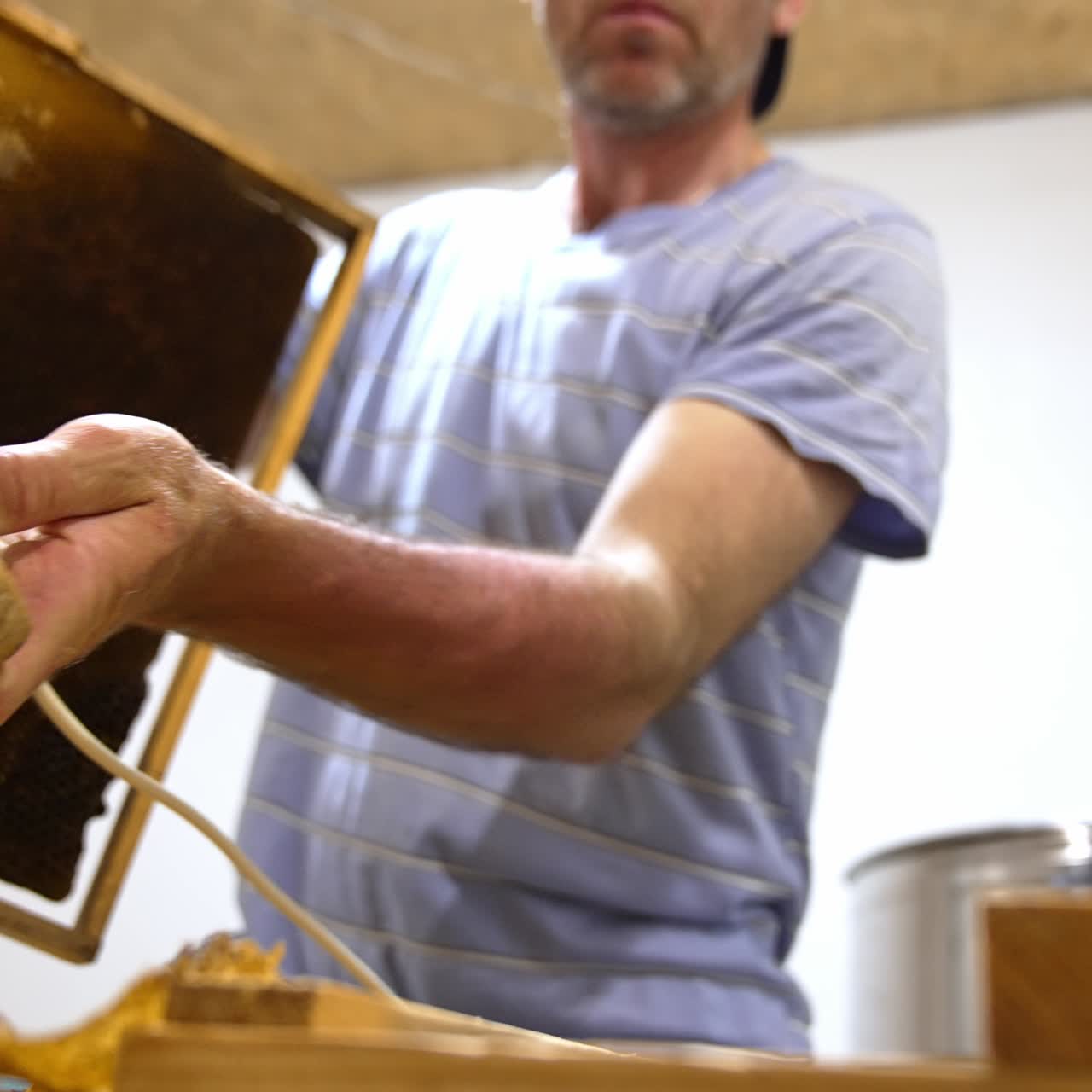 Apiarist holding a special tool in hands to uncover the sealed cells. Man prepares frames for removal of honey