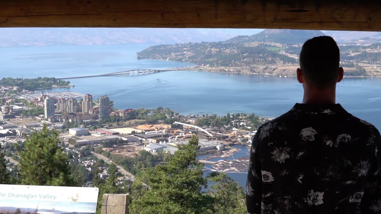 hombre mirando una bonita vista de una ciudad desde un pabellón junto a un lago en la montaña knox en kelowna, bc, canadá