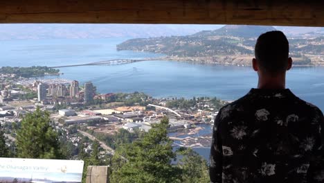 man looking at a nice view of a city from pavilion beside a lake at knox mountain in kelowna, bc, canada