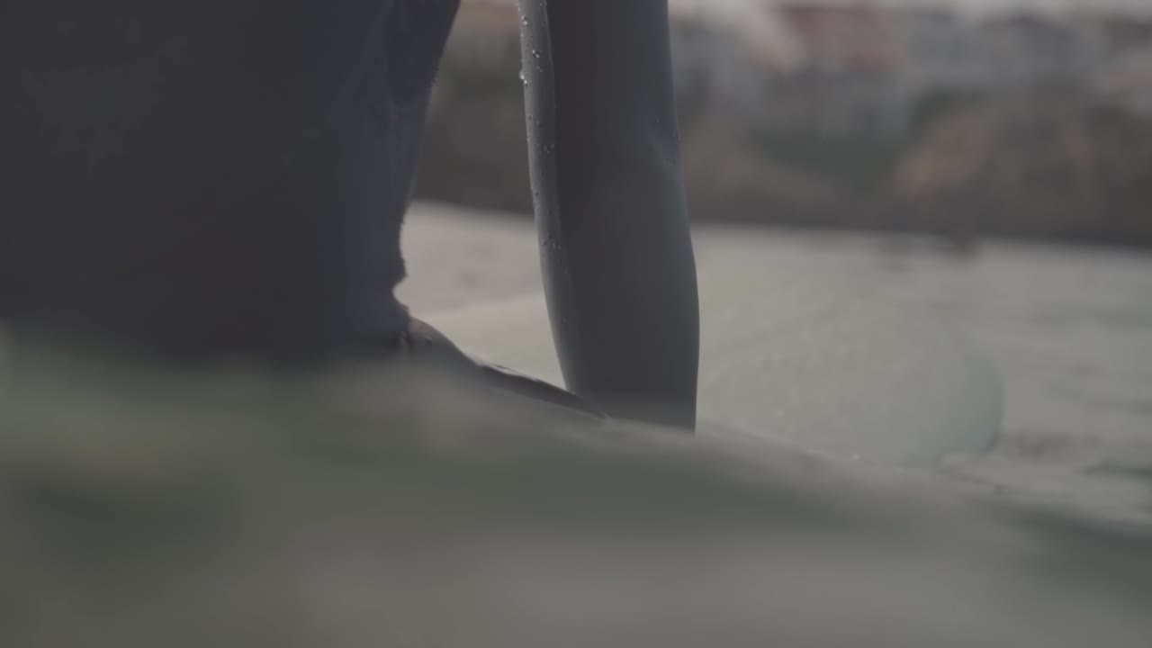 крупный план серфингиста в гидрокостюме, сидящего на доске, замедленная съемка на уровне поверхности воды