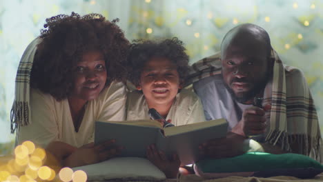 portrait of african american family with flashlights and book on bed
