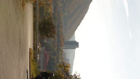 Brand-new-red-sporty-scooter-driving-uphill-in-mountain-road-in-Banska-Bystrica,-a-town-in-Central-Slovakia---vertical-establishing-shot