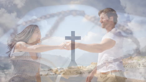 animation of cross on mountain, rosary on bible over caucasian couple dancing on beach