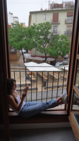 woman relaxing at window during rainy day