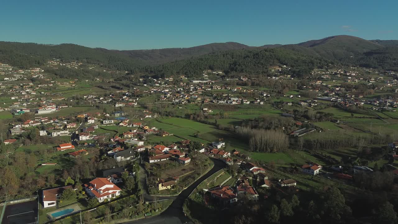Cinematic slow push-in drone shot establishing the town of Arouca, Portugal. Aerial view approaching traditional red-roofed buildings nestled in the green hills of the Aveiro district