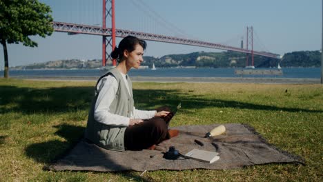 woman working on laptop in park by the bridge