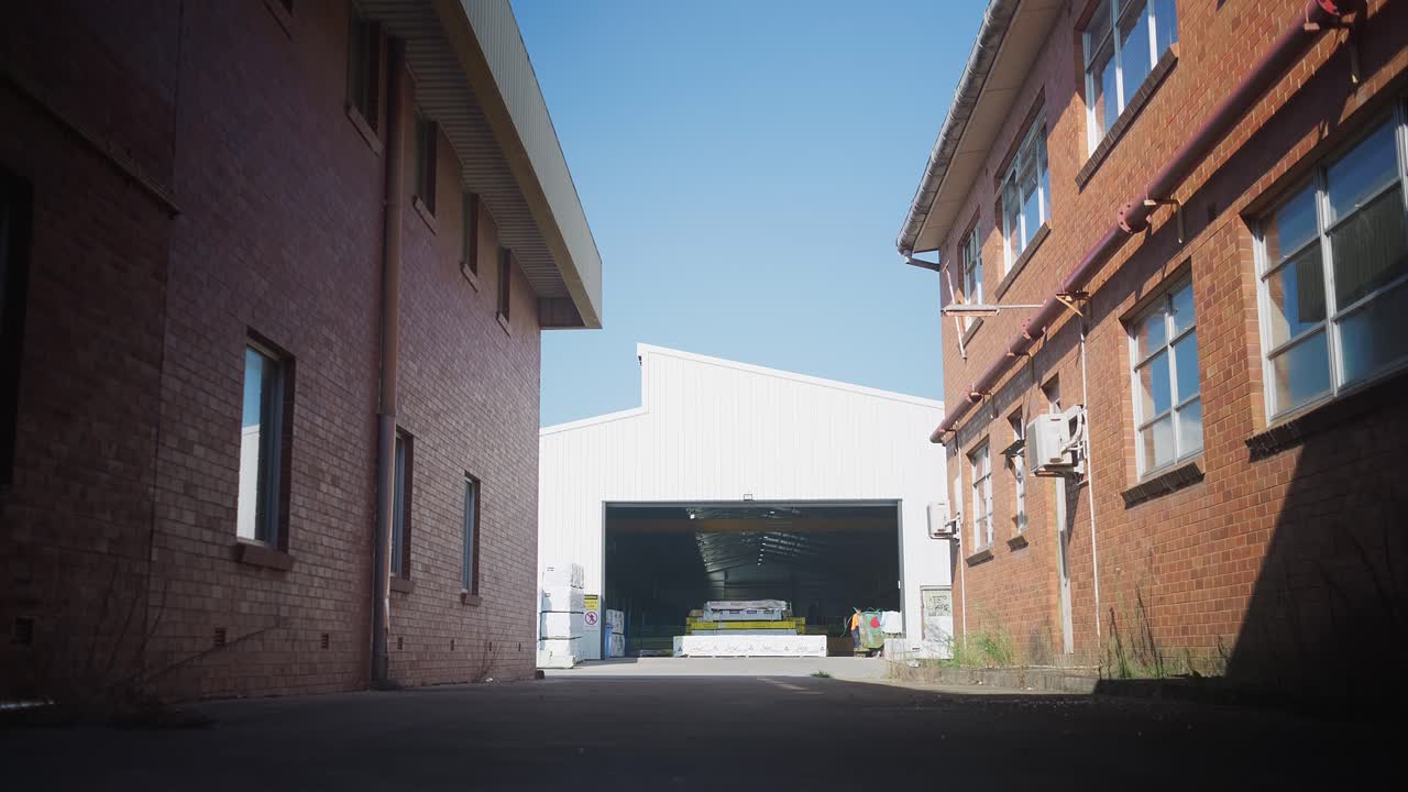 Fast stativskudd av et moderne lager innrammet av et eldre lager i forgrunnen, med en enslig arbeider som beveger seg i bakgrunnen, og skaper en industriell kontrastscene.