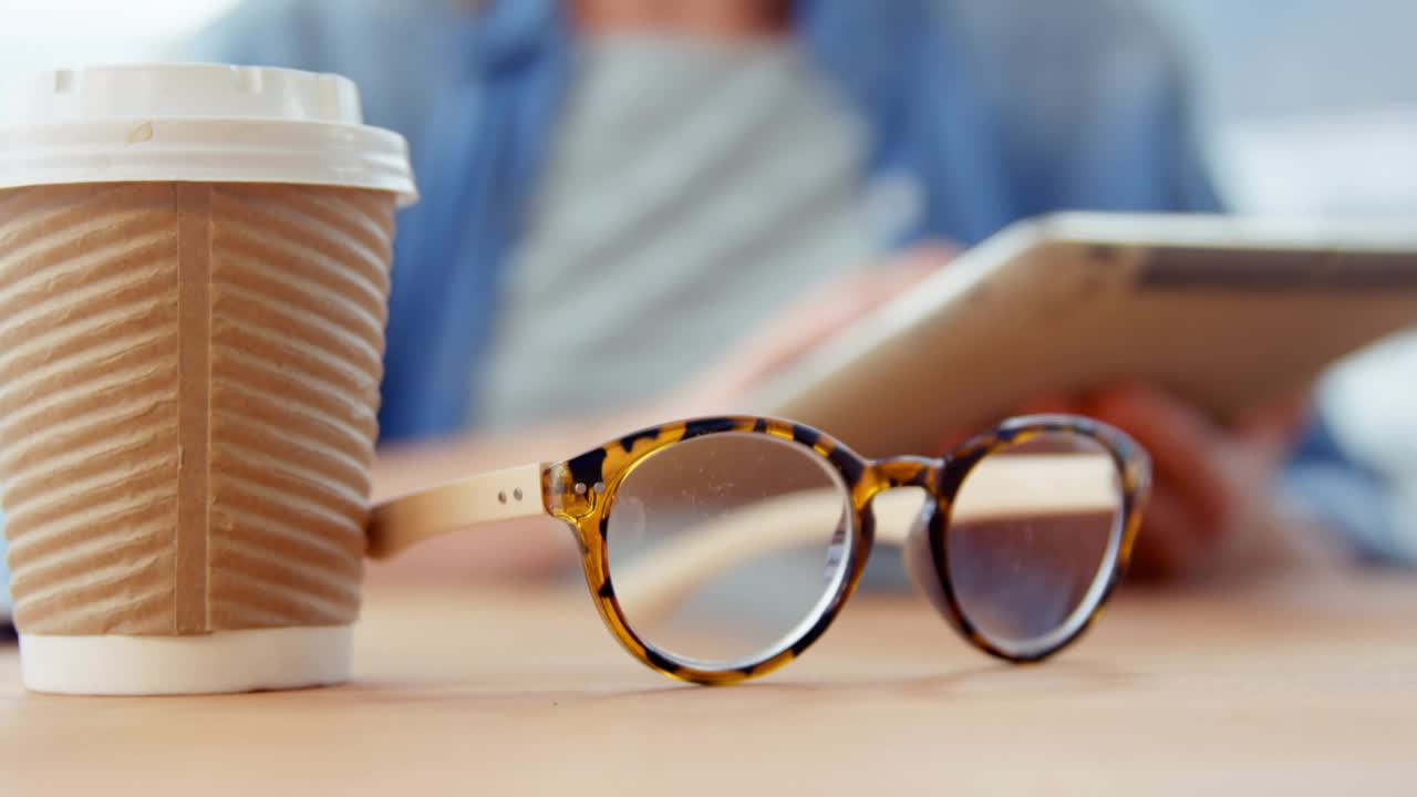 Woman tapping tablet, launching analytics bars and waveform over screen, cup and glasses foreground