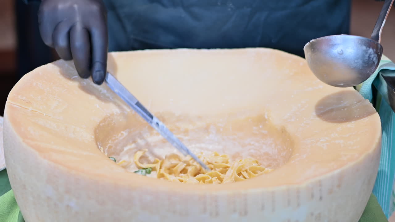 Man taking out the pasta from a heated parmesan wheel at a restaurant