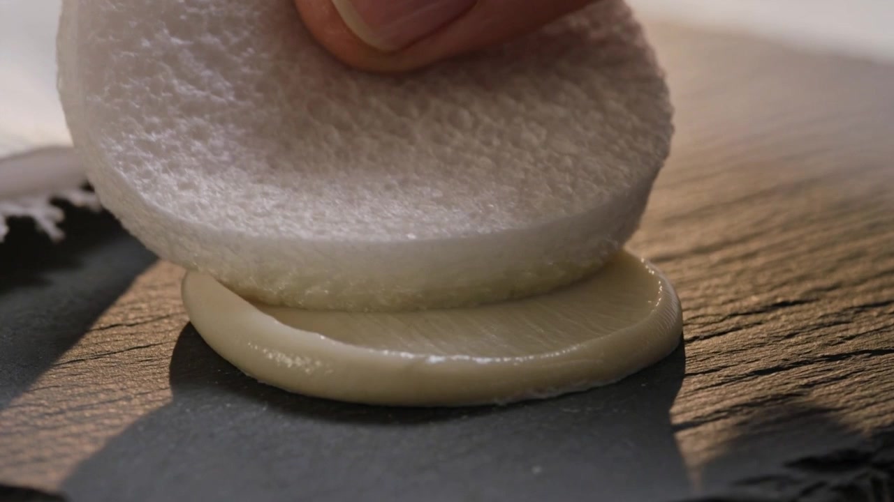 Pressing bare hand lowering textured pad onto batter on kitchen board, cloth behind, forming disk