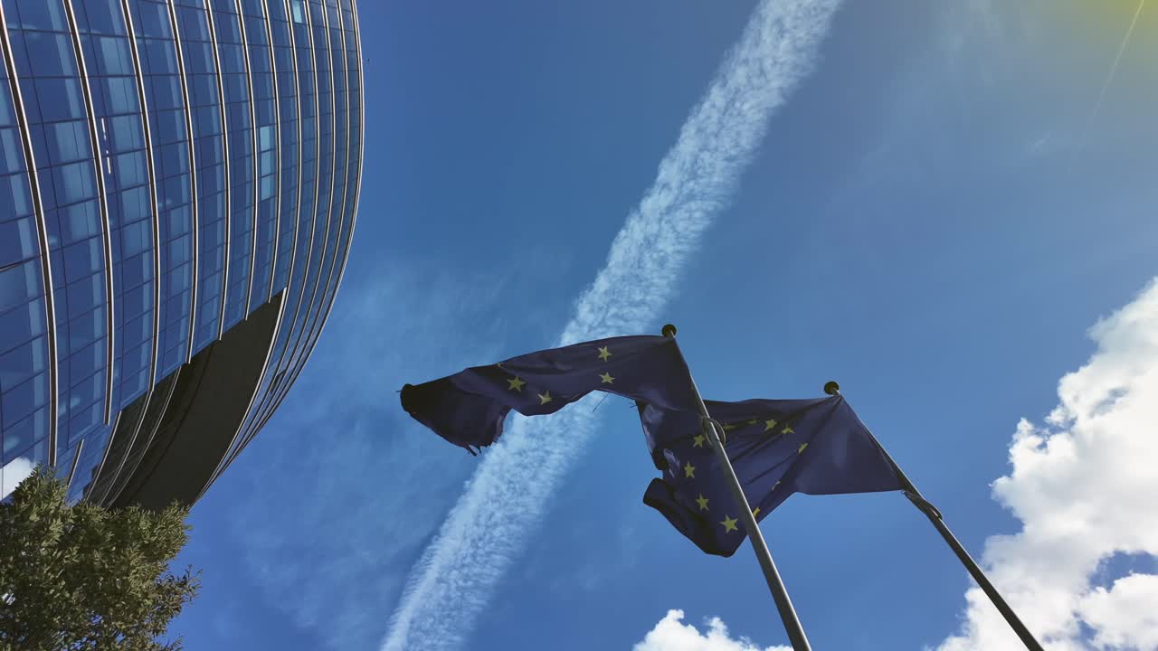 European Union flags fluttering in sunlight against blue sky with the Lex Building in Brussels’ European Quarter