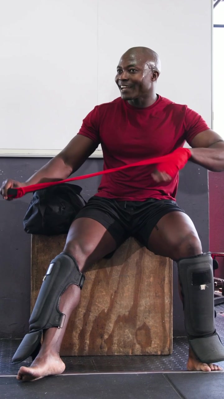 Vertical video: Wrapping red wrap, post-sparring red-shirted athlete fixing guard on box with pad