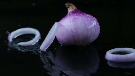 close up view of onions rings falling on an onion on black background