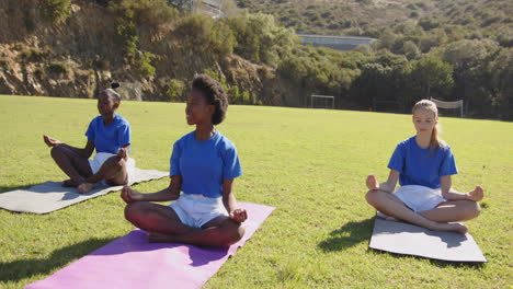practicing yoga on mats, girls meditating outdoors in school field