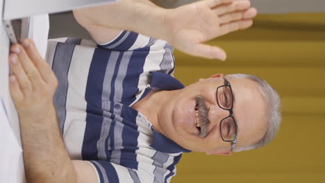 Vertical-video-of-Home-office-worker-old-man-waving-at-camera.