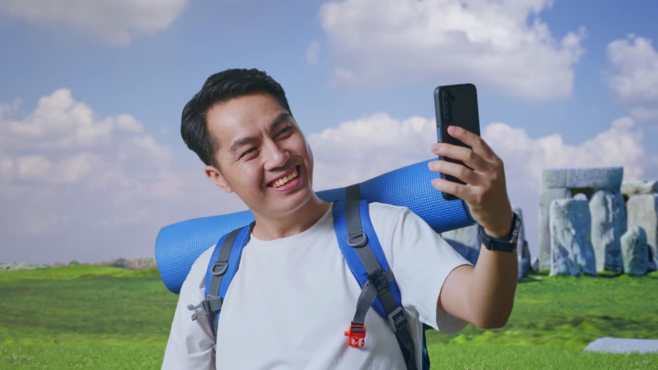 Close Up Of Asian Male Hiker With Mountaineering Backpack Showing Peace And Thumbs Up Gesture While Taking A Selfie While Traveling In Stonehenge