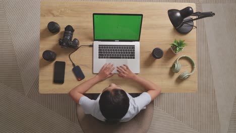 top view of asian woman video editor drinking coffee while using green screen laptop and smartphone next to the camera in the workspace at home