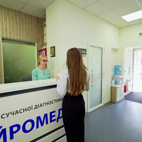 young woman in modern clinic. female patient coming into the hospital and talks to the receptionist. visit to the doctor.