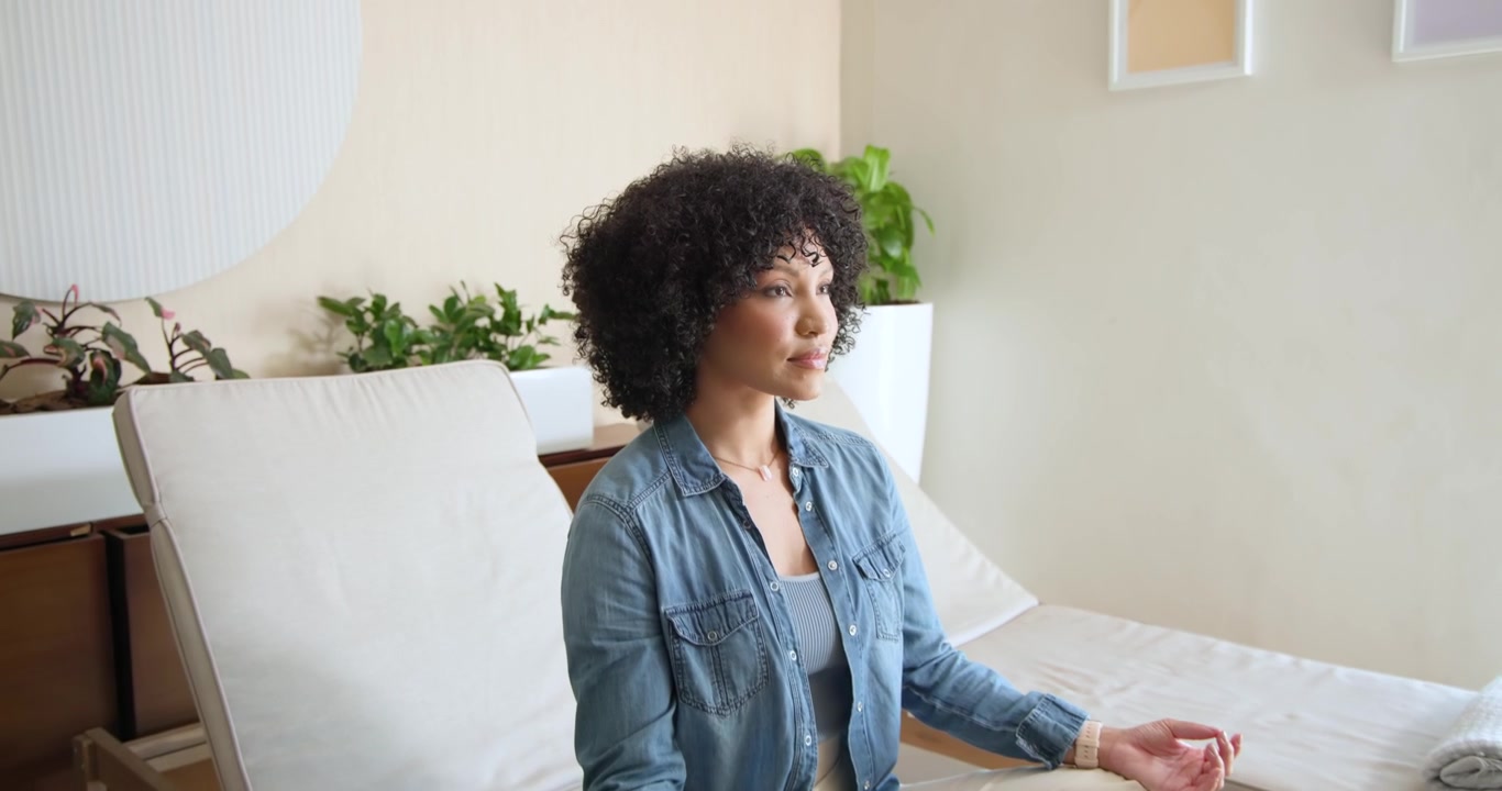 Donna afroamericana che chiude gli occhi, respira e medita per trovare la calma, in jeans su una chaise longue con il telefono.