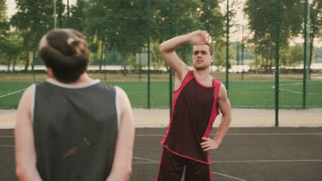 dos jugadores de baloncesto masculinos estirándose en una cancha de baloncesto al aire libre antes de jugar