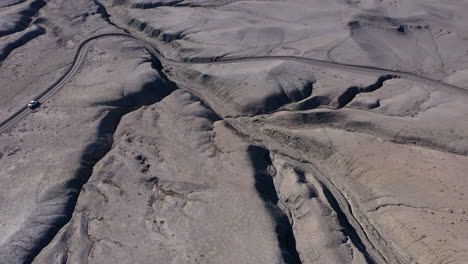 white truck travels on unpaved road in desert, high angle drone view