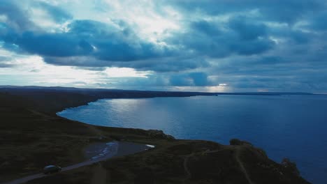 aerial shot of some cornish cliffs with a car driving along in shot