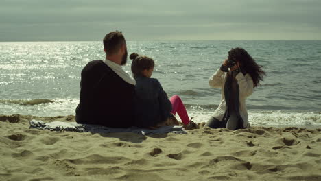 young family taking pictures on sunny day beach. mom dad child photographing sea