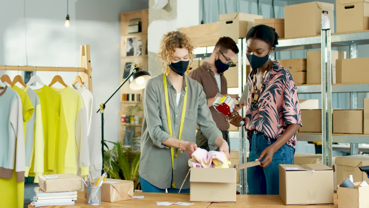 백인 남자가 노트북에 타이핑을 하는 동안 소포를 포장하는 옷가게에서 일하는 백인과 아프리카계 미국인 젊은 여성